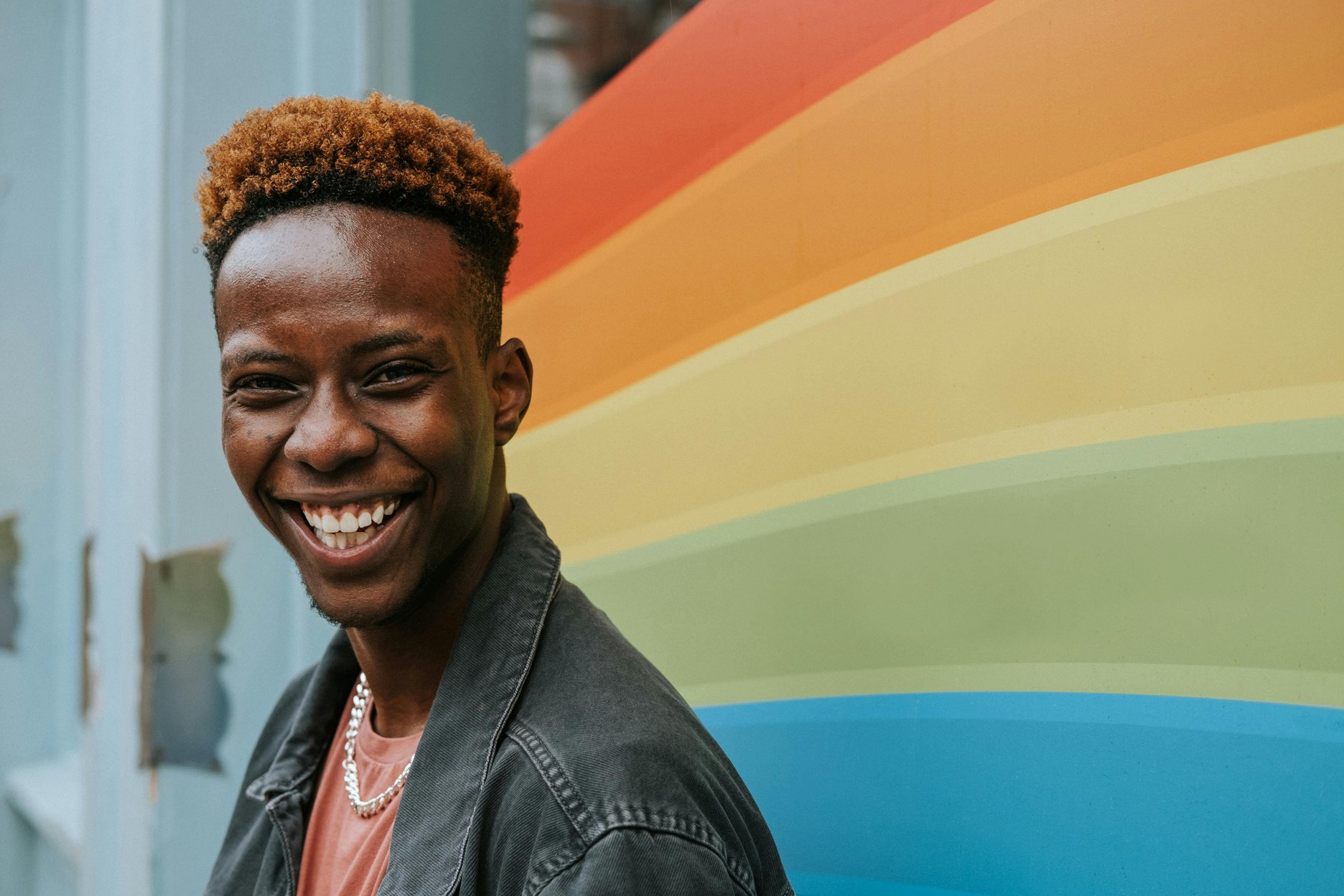 a smiling person in front of a rainbow colored wall