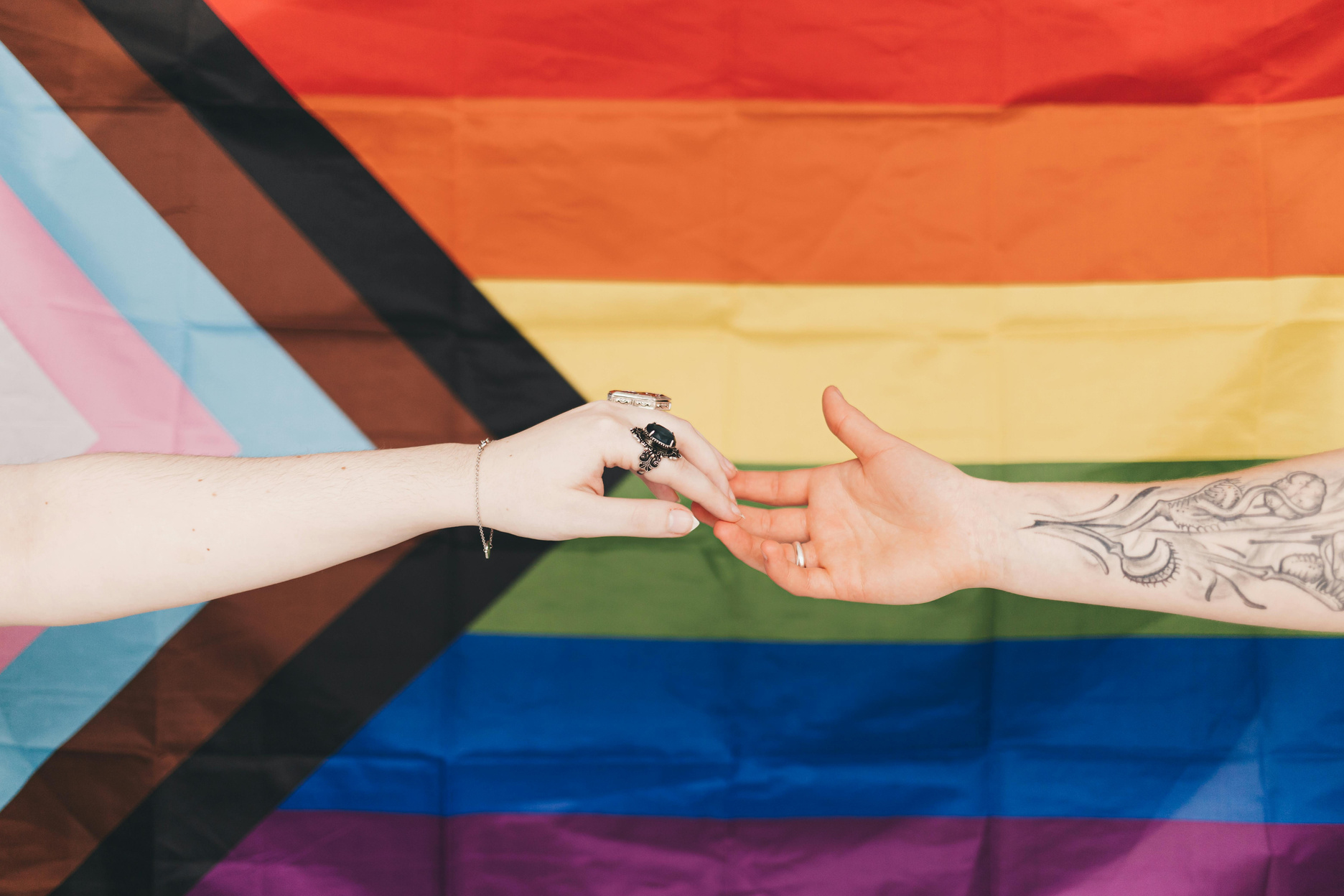 two people holding hands in front of a rainbow flag